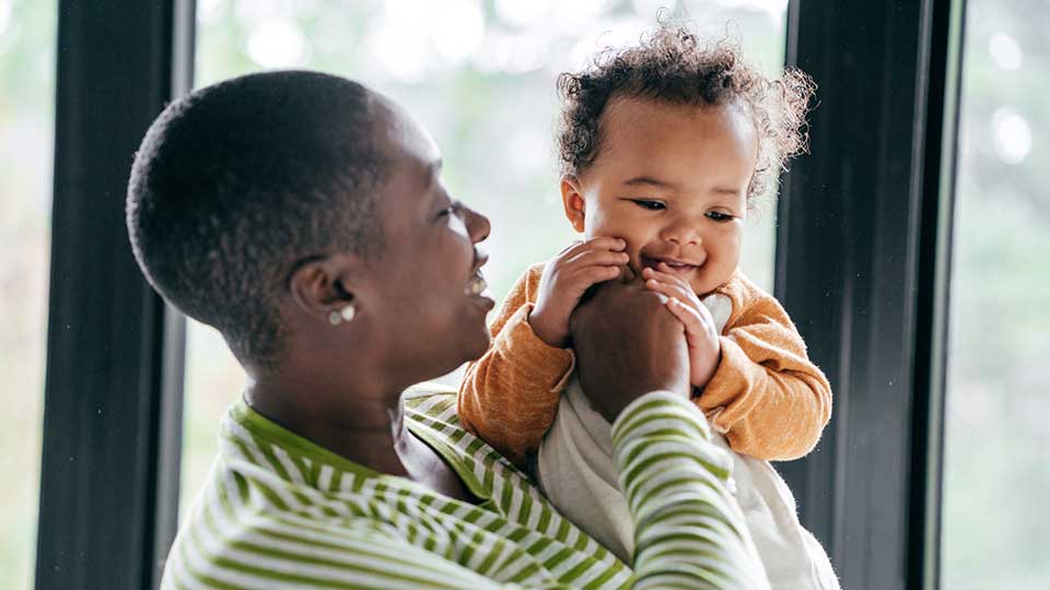 A smiling baby chewing on a parent’s fingers while being held, a typical teething comfort behavior that helps soothe sore gums.