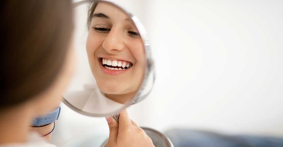 Teen girl at the pediatric dentist, looking and smiling at her reflection in a mirror.