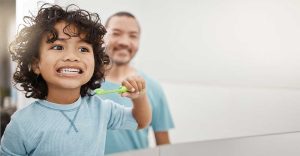 Young child brushing teeth with father