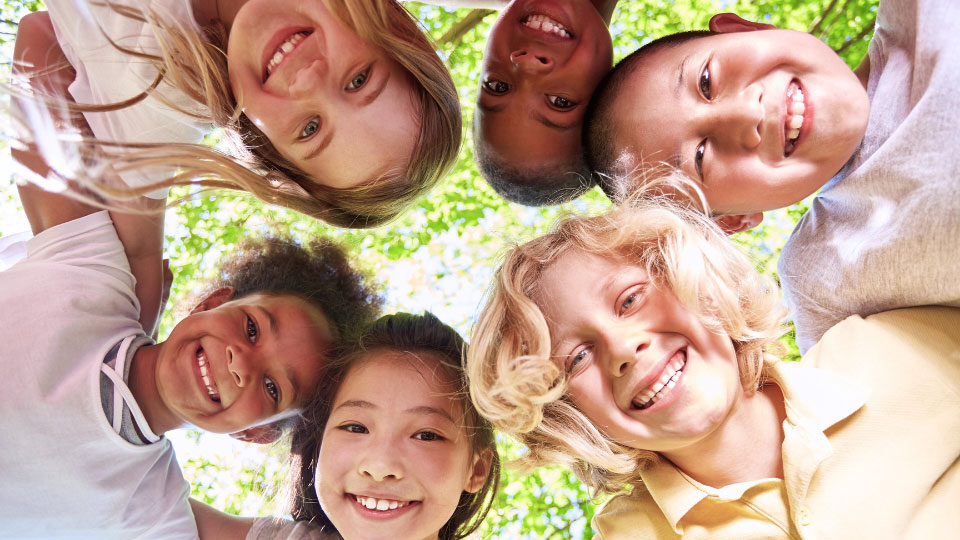 Group of diverse, smiling children looking down at the camera under a tree – promoting healthy kids' smiles for pediatric dental care in Fleming Island, FL