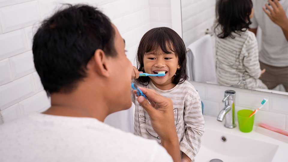 Father and young daughter brushing teeth together