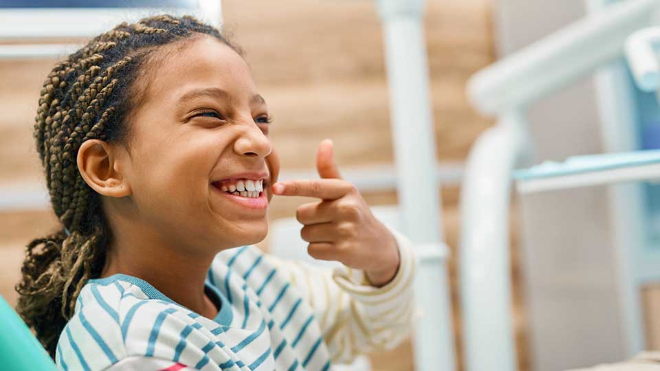 Young African American girl pointing to her teeth at pediatric dentists office