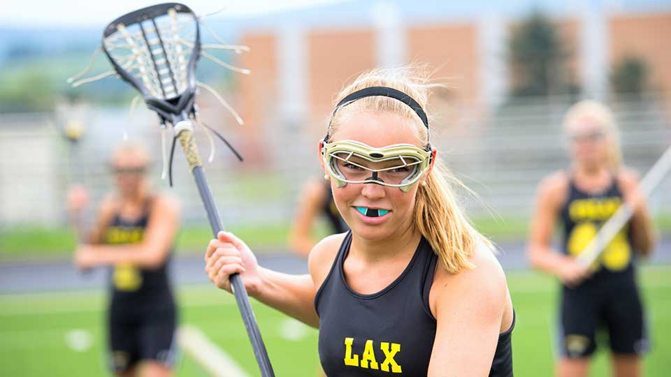 teen girl playing lacrosse wearing a protective sports mouthguard