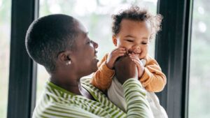A smiling baby chewing on a parent’s fingers while being held, a typical teething comfort behavior that helps soothe sore gums.